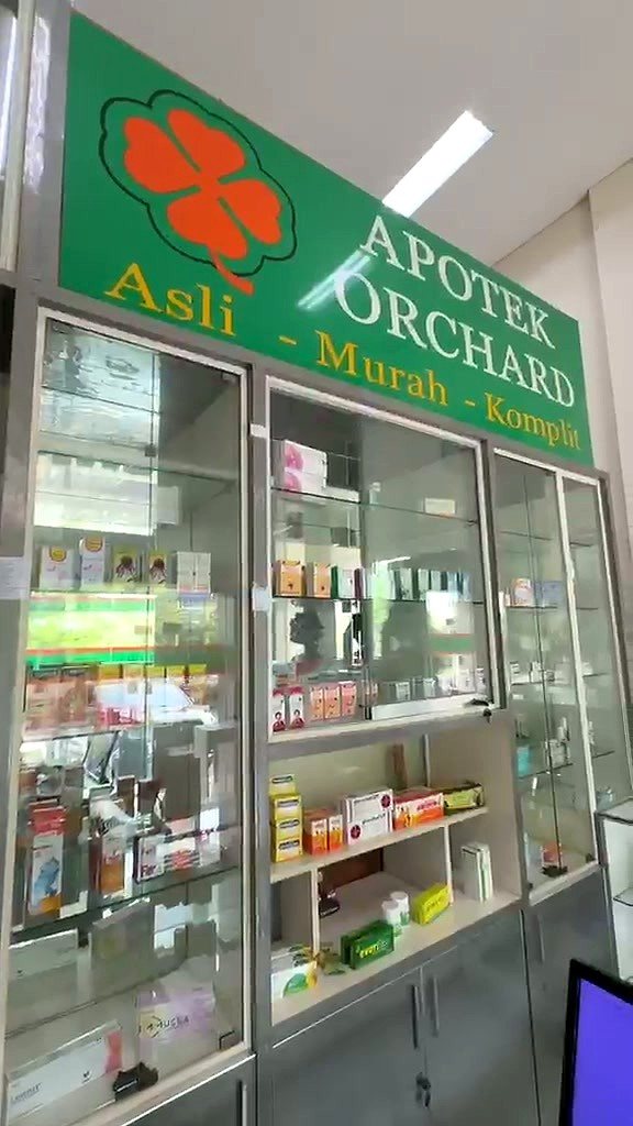 Inside Apotek Orchard: the green signboard with its orange clover above glass cabinets of medicines